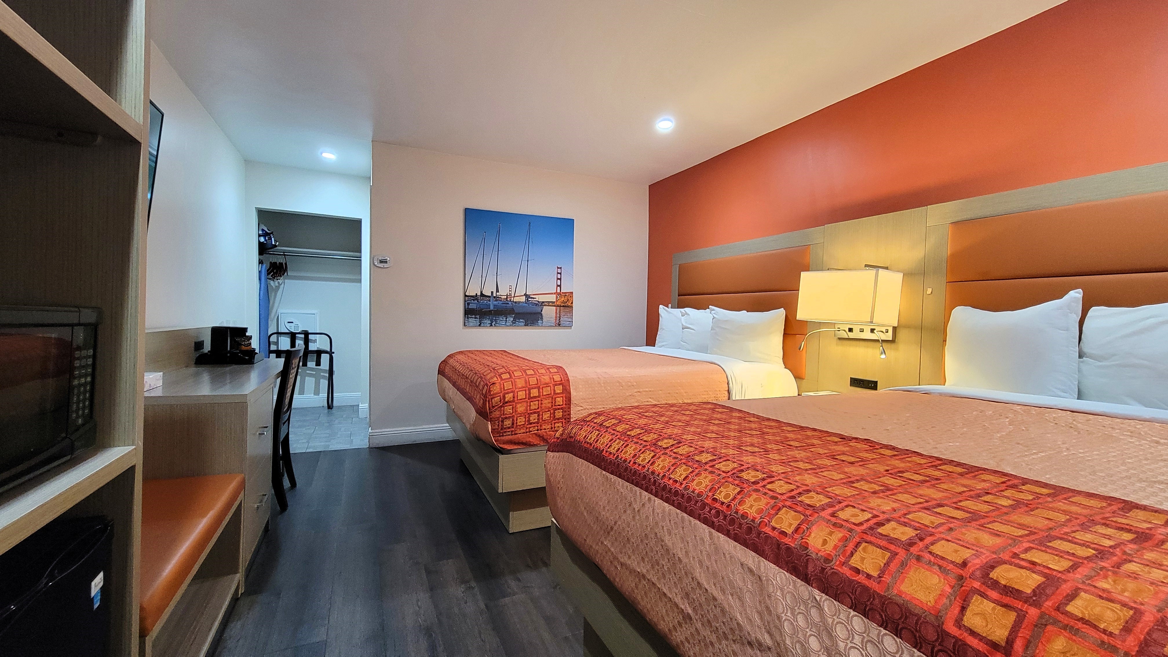 A hotel room with two beds, a desk, a TV, and a closet.