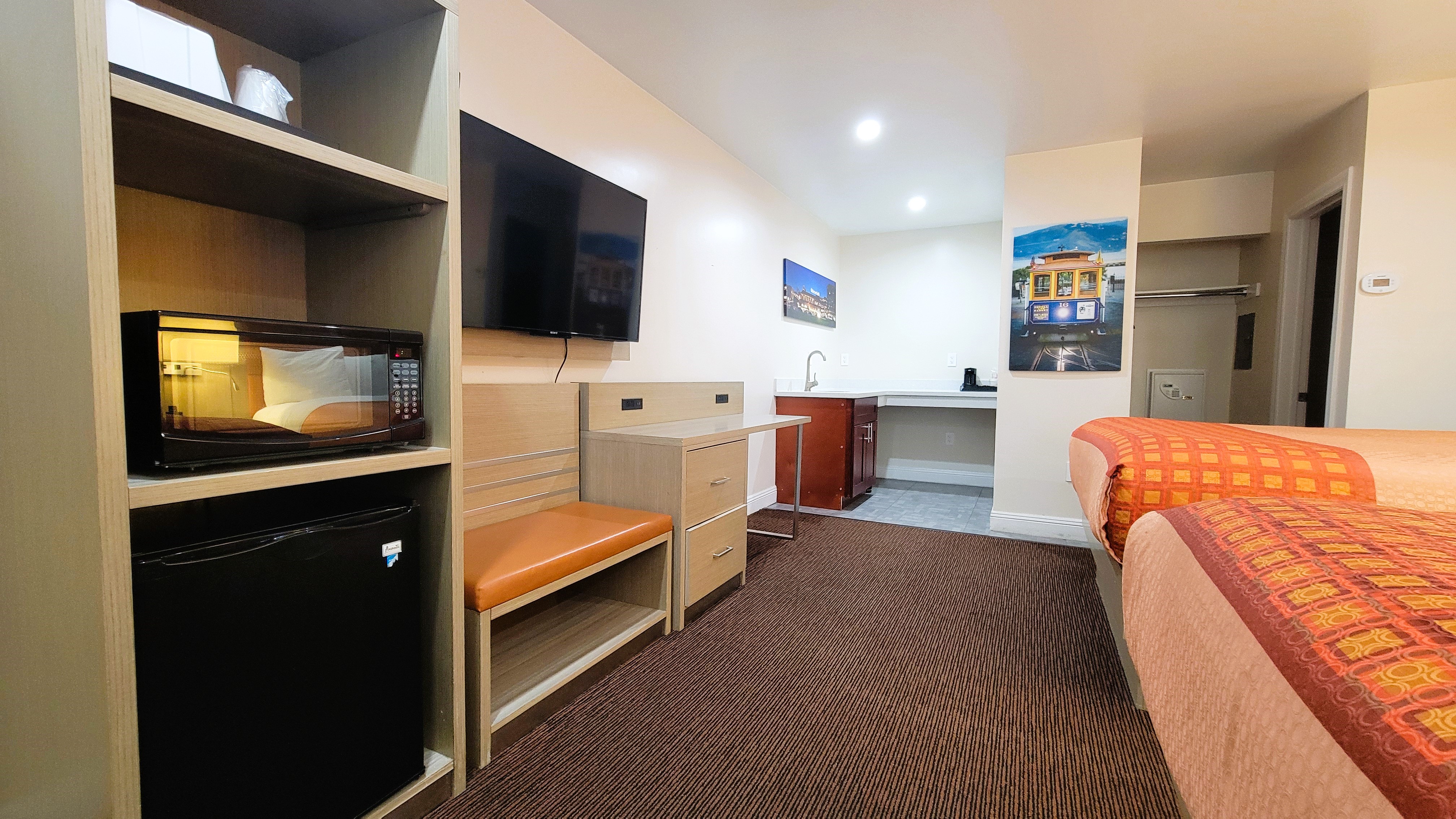 A hotel room with a kitchenette, microwave, mini fridge, and queen bed.
