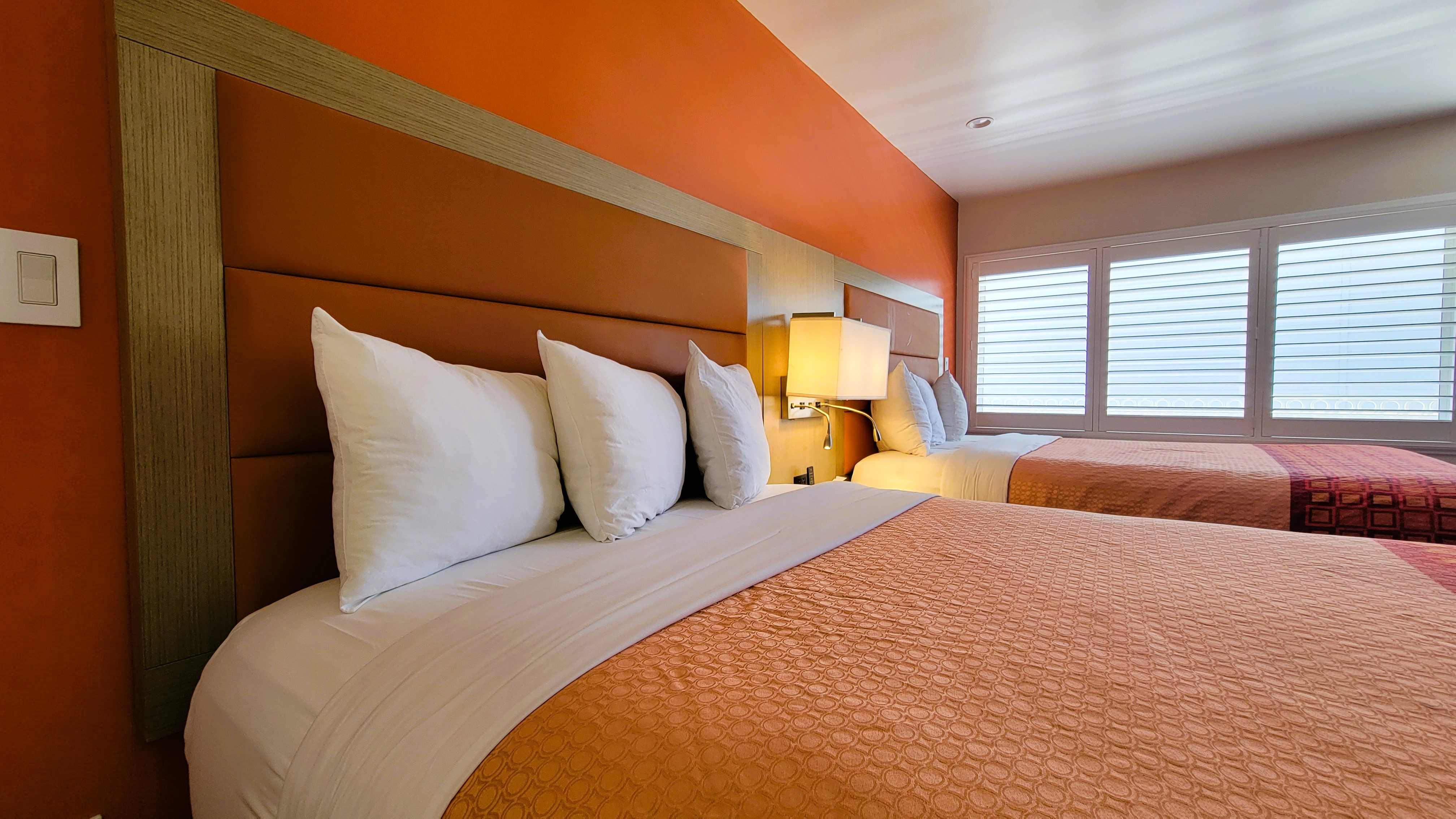 A hotel room with a large bed, orange walls, and a window with blinds.