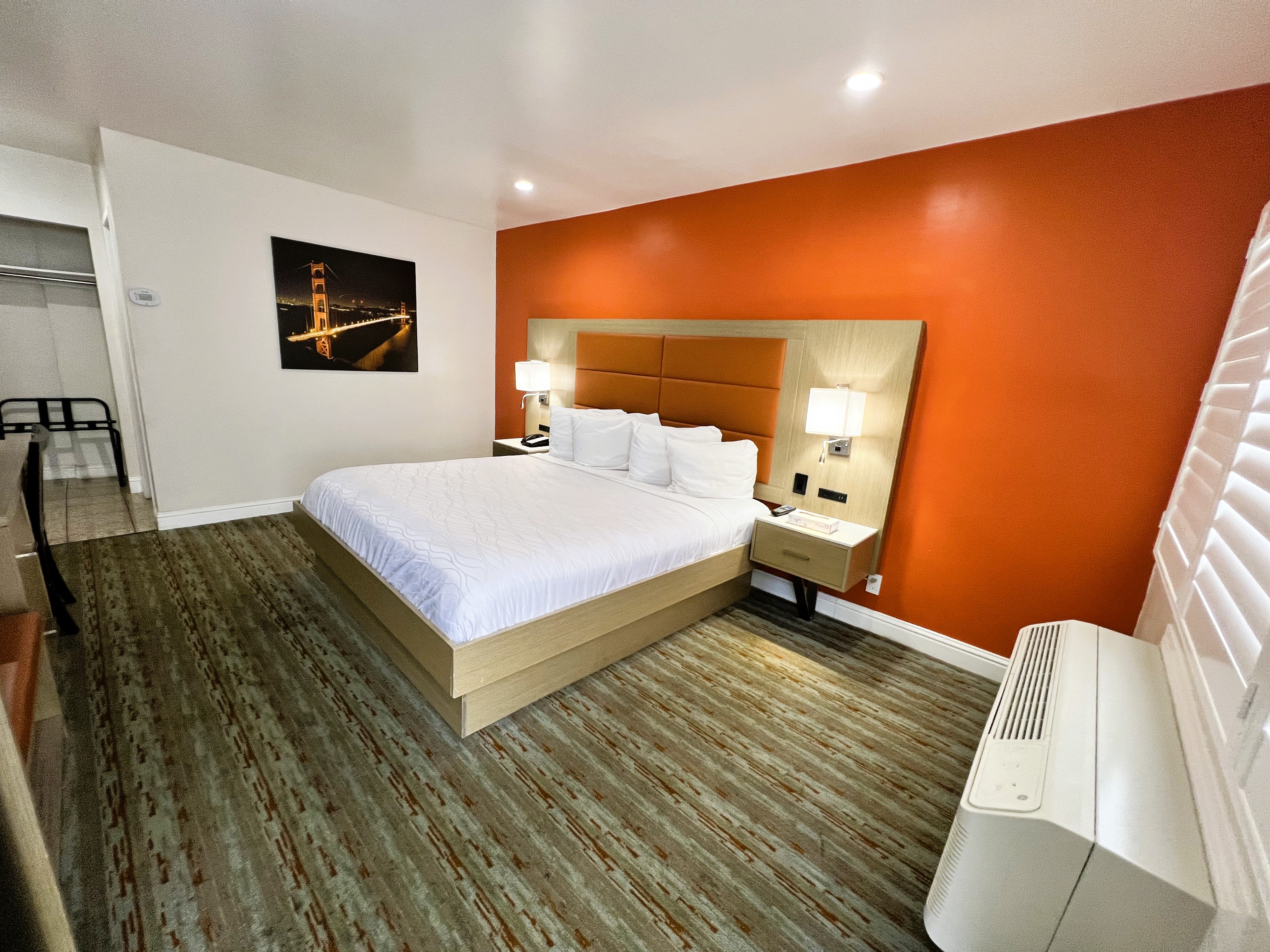 A hotel room with a large bed, two nightstands with lamps, and a window with blinds.