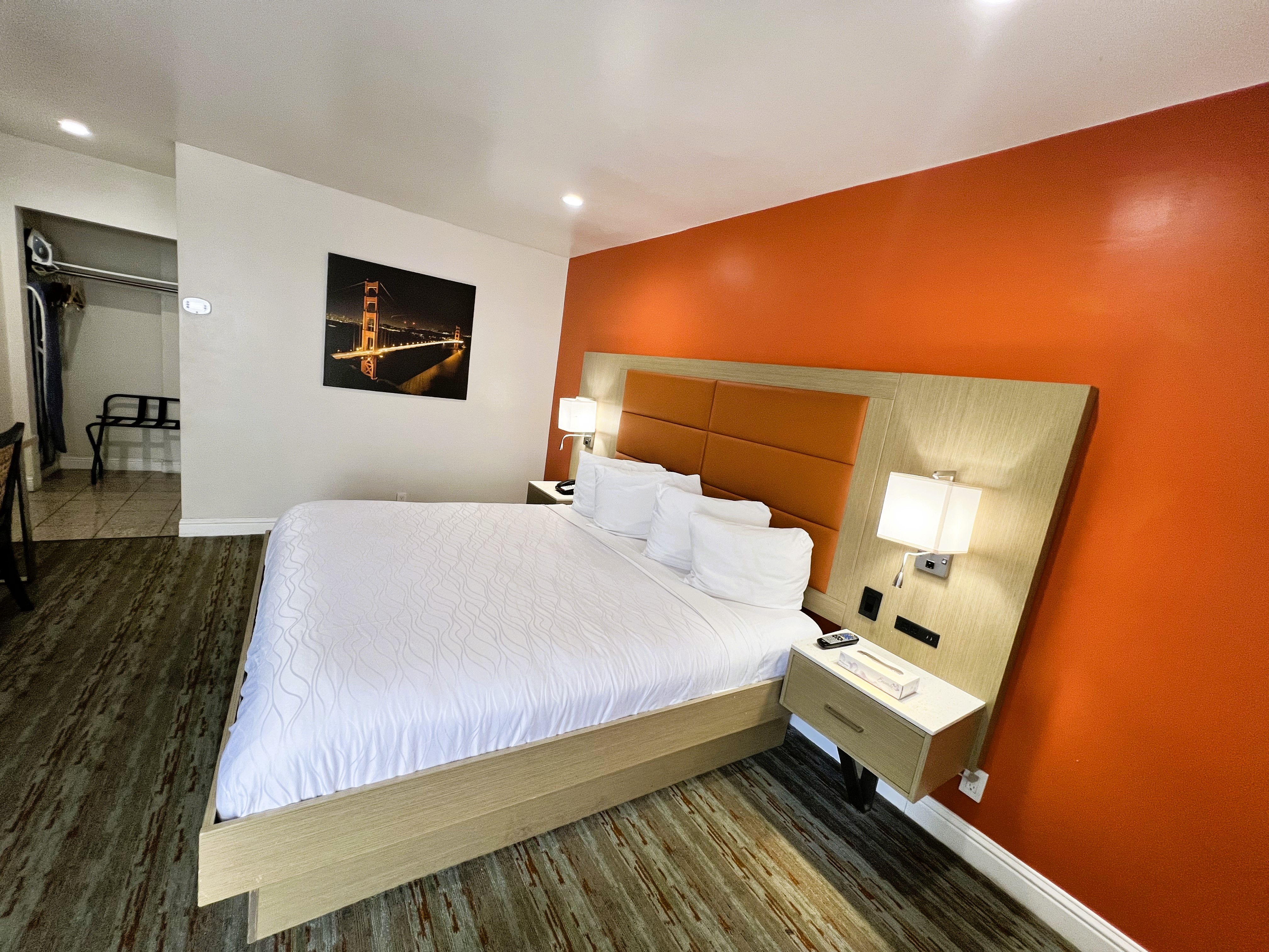A wide-angle view of a hotel room with a king-sized bed, orange accent wall, and wooden headboard.