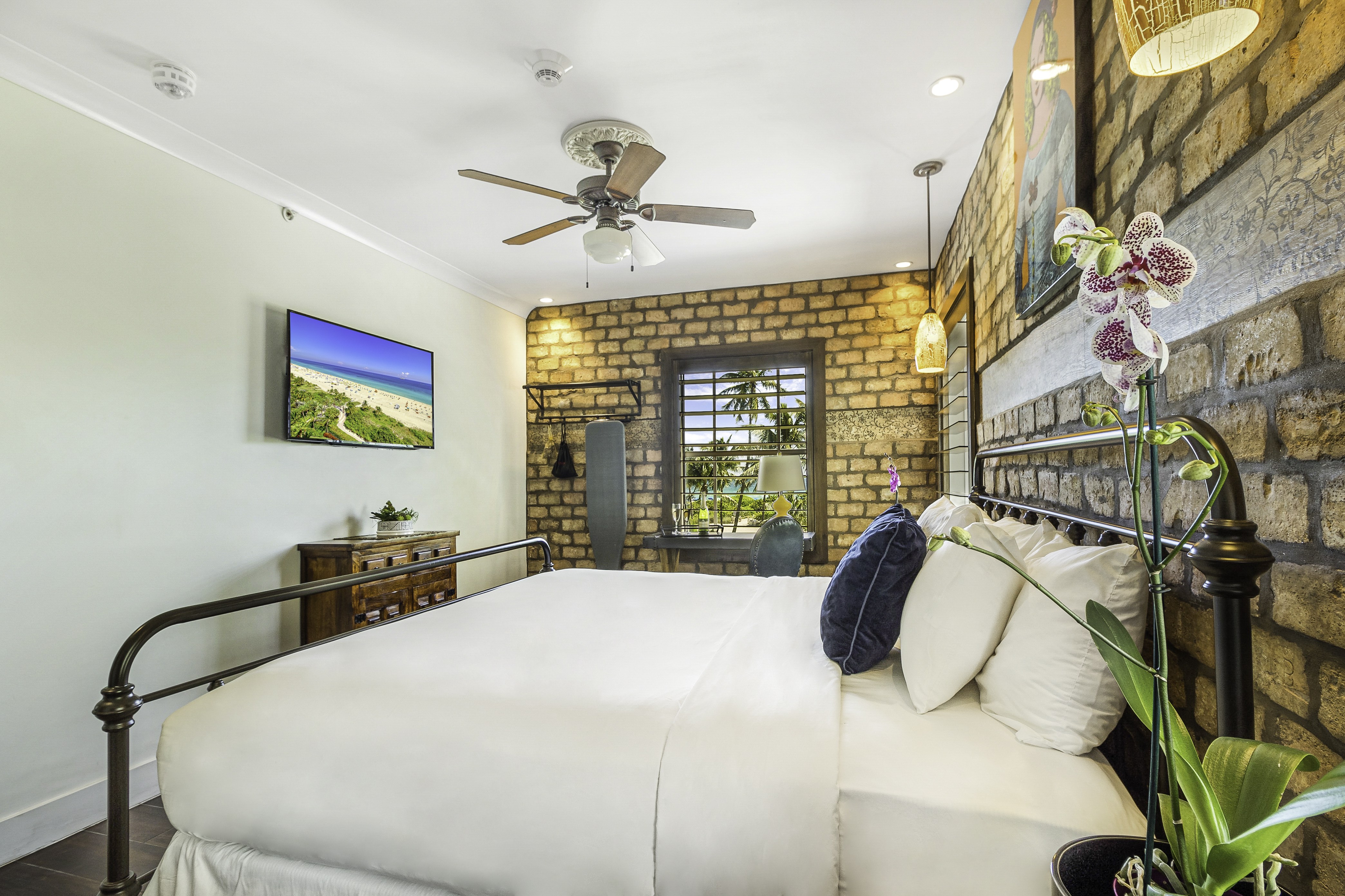 A hotel room with a bed, window, TV, and ceiling fan